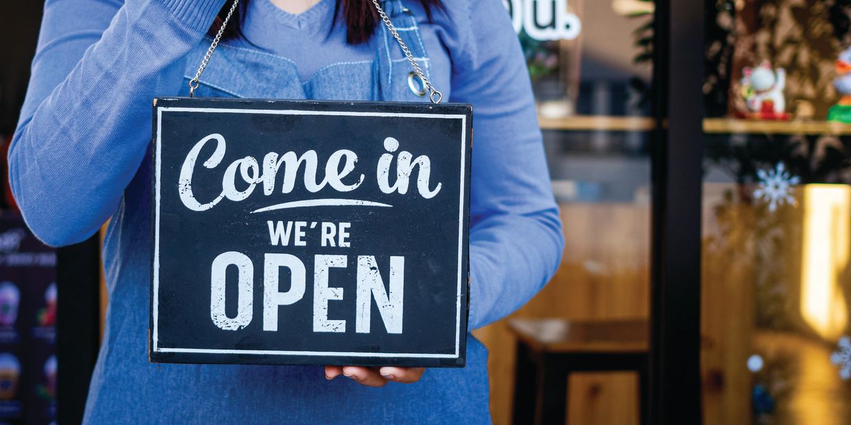 Person holding a 'Come in, we're open' sign.