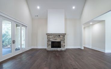 Spacious empty room with stone fireplace and dark hardwood floors.