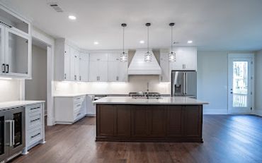 Modern kitchen with white cabinets and a dark island under pendant lights.