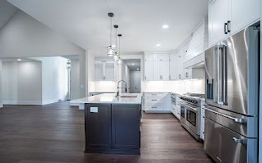 Modern kitchen with white cabinets, dark island, and stainless steel appliances.
