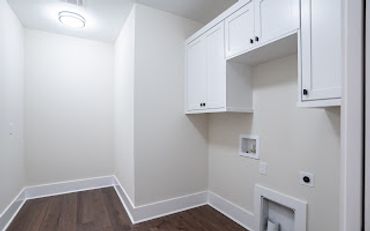 Empty laundry room with white cabinets and dark flooring.