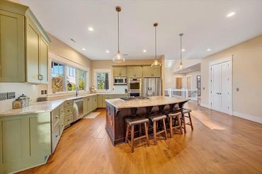 Spacious kitchen with green cabinets, large island, and wooden stools.