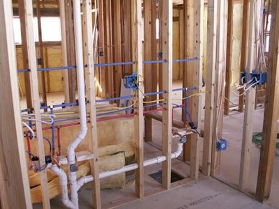 Exposed wooden framing with plumbing and electrical wiring during house construction.