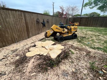 A stump grinder machine next to a freshly ground tree stump in a backyard.