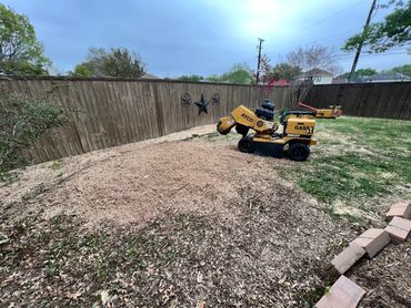 Yellow wood chipper machine in a backyard with wood chips spread around.