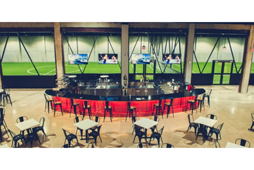 Modern sports bar with a vibrant red counter and outdoor soccer field view.