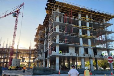 Partially constructed multi-story building with workers and crane at sunset.
