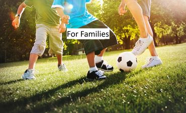 Children and an adult playing soccer together outdoors on a sunny day.
