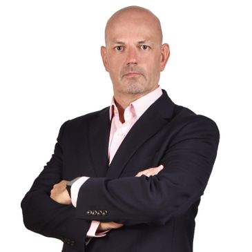 Confident bald man in a dark suit with arms crossed.
