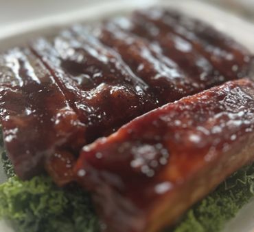 Close-up of glazed barbecue ribs on a bed of leafy greens.