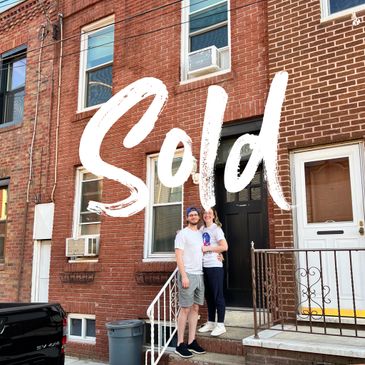 Happy couple standing in front of their sold brick townhouse.