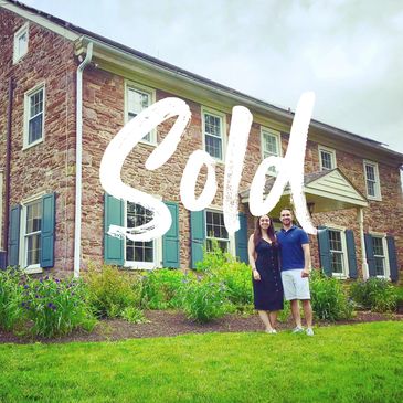 Happy couple standing in front of their newly sold house with "Sold" text overlay.