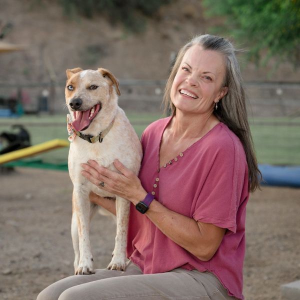 A smiling woman in a pink shirt holds a happy dog outdoors.