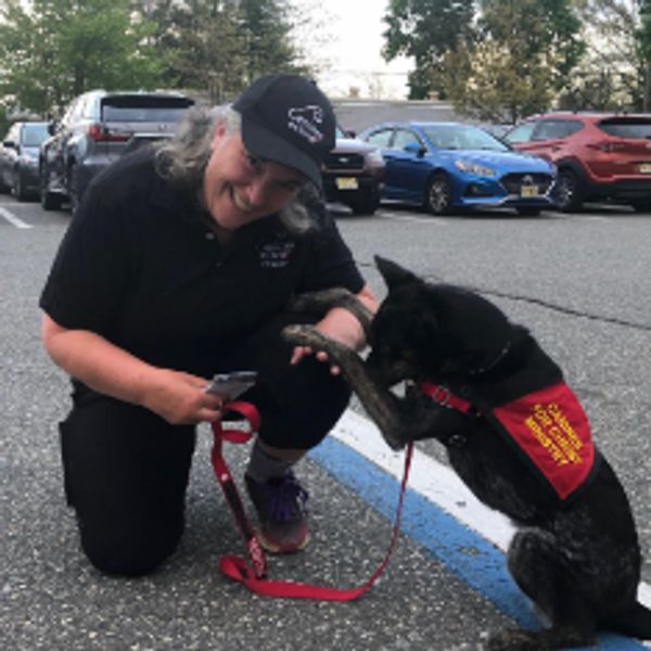 A woman smiles while training a service dog in a parking lot.