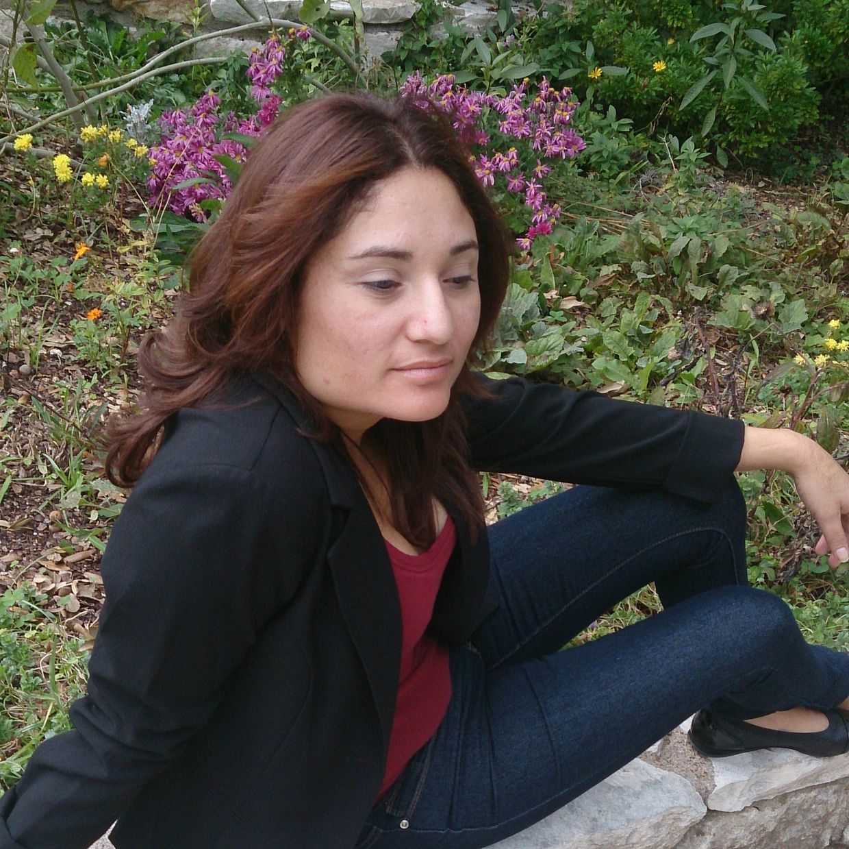 Woman sitting on a stone wall in a garden.