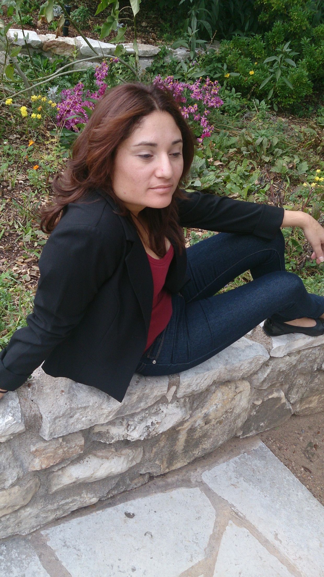 Woman sitting on a stone wall in a garden.