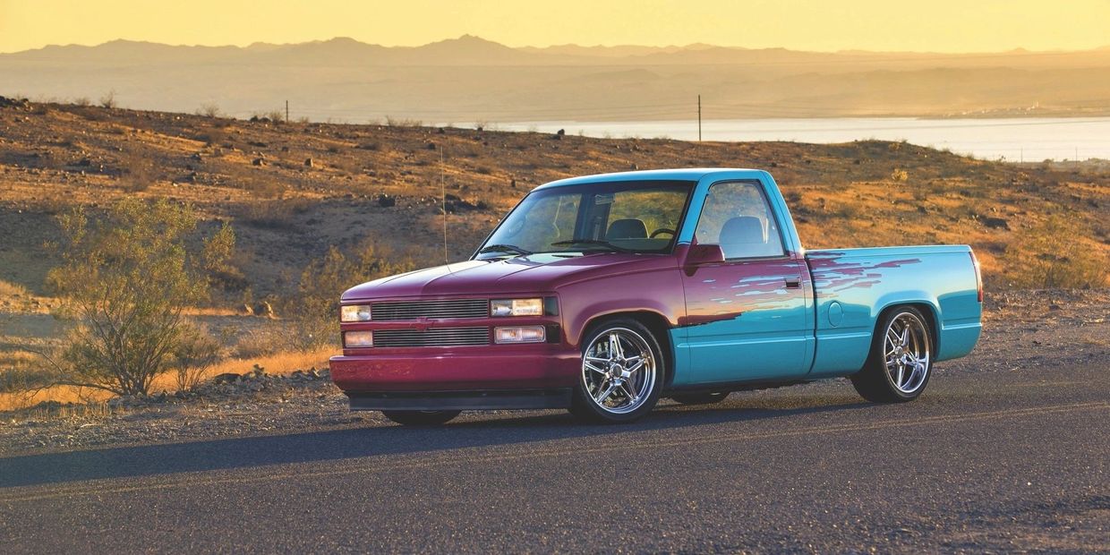 Custom two-tone pickup truck parked on a desert road at sunset.