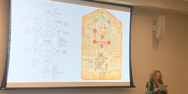 A woman presenting her conference paper with a slide about Kabbalah in the background