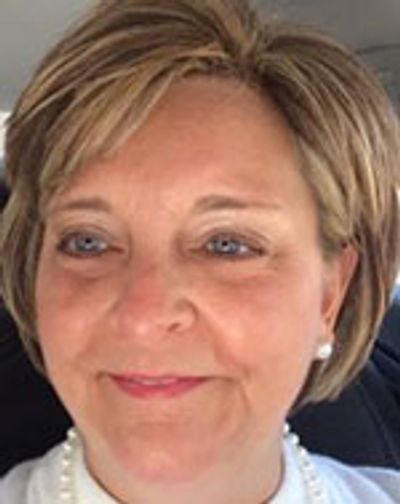 Smiling middle-aged woman with short blonde hair and pearl earrings.