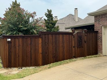 A wooden fence and gate enclosing a suburban yard with flowering trees behind.