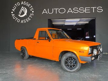 Bright orange vintage pickup truck showcased indoors at Auto Assets.