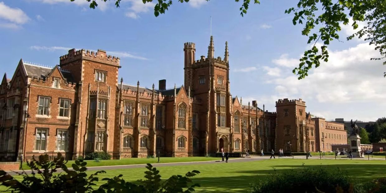 Historic red-brick university building with manicured lawns under a sunny sky.