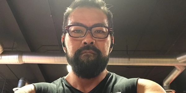 Bearded man wearing glasses and a sleeveless shirt at a gym.