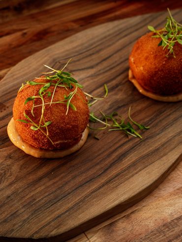 Two crispy breaded appetizers garnished with greens on a wooden board.