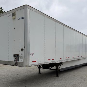 White cargo trailer parked on a concrete surface under a cloudy sky.