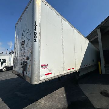 A white semi-trailer truck parked at a loading dock under clear skies.