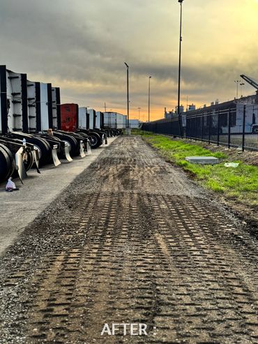 A newly leveled dirt path with tire tracks beside parked trucks at sunset.