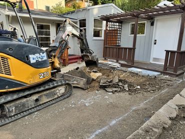 Excavator breaking up old concrete in a driveway renovation.