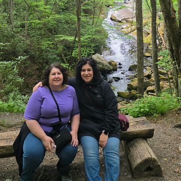 Two women sitting on a wooden bench in the forest.