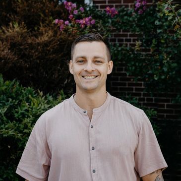 Smiling man in a pink shirt outdoors.