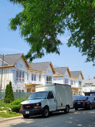 White GMC box truck parked near new houses under construction on a sunny day.