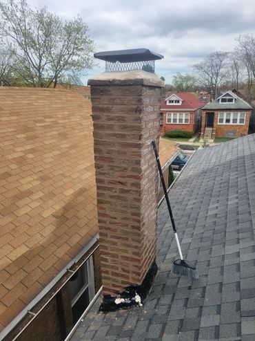 A chimney on a rooftop with a broom leaning against it.