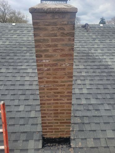 Brick chimney on a shingled roof with a ladder.