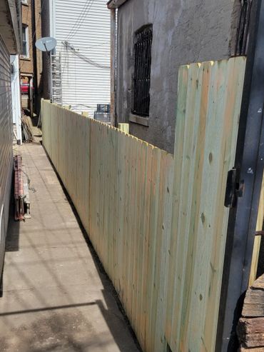A newly installed wooden fence along a narrow alley between buildings.