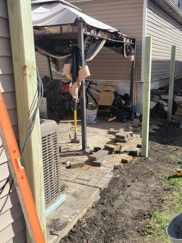 Backyard patio under renovation with stacked bricks and gardening tools.