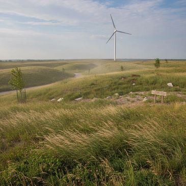 A wind turbine stands tall over a grassy, rolling landscape under a partly cloudy sky.