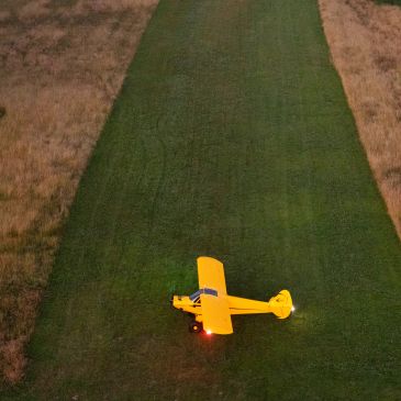 A yellow plane on a grass runway at dusk.