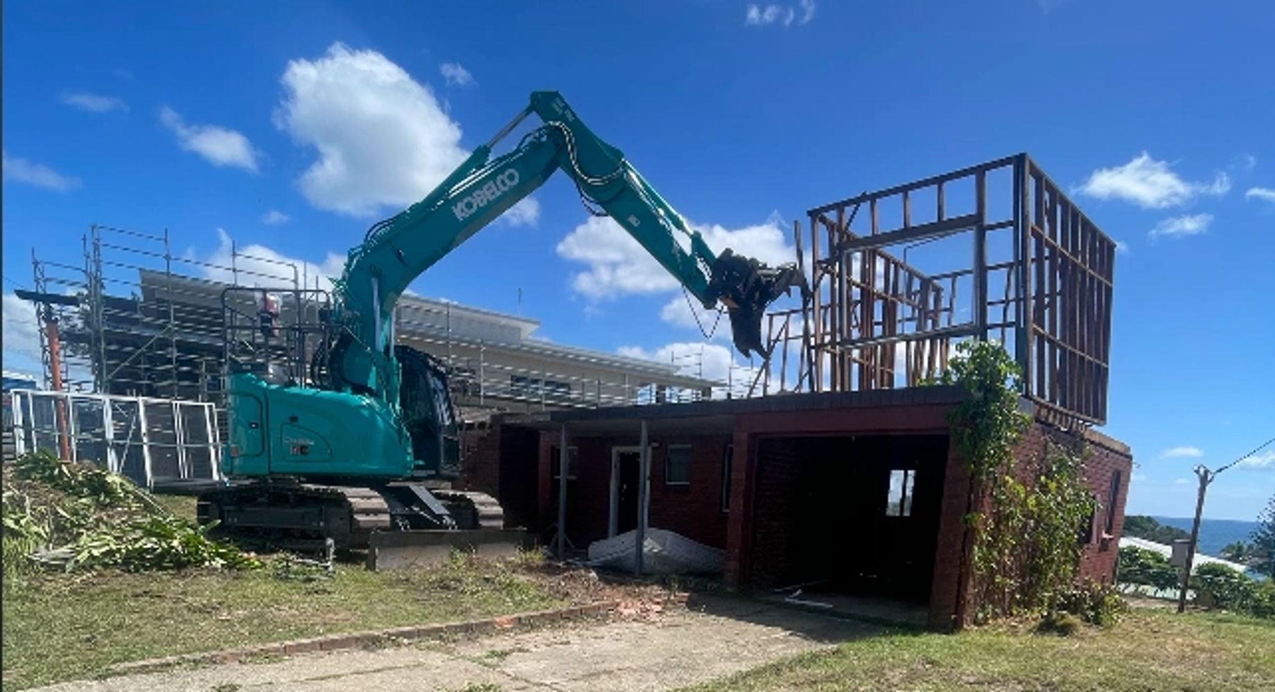Excavator demolishing part of a building under clear blue sky.