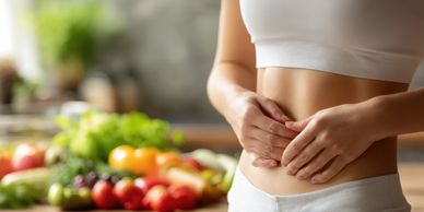 Woman holding her stomach with fresh vegetables in the background.
