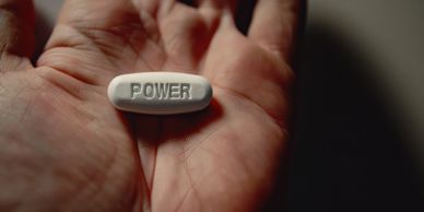 A white pill with the word 'POWER' held in an open hand.