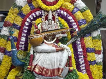 Idol of goddess Saraswati decorated with colorful flowers and holding a veena.