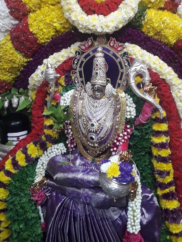 Ornate deity statue adorned with colorful flower garlands and jewelry.