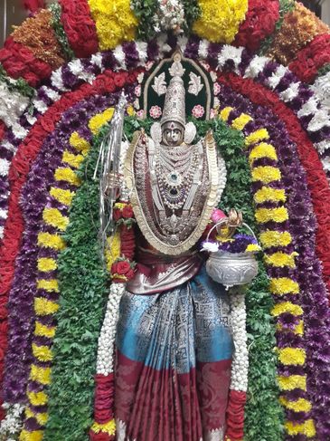 Ornate deity statue adorned with colorful flower garlands and intricate jewelry.