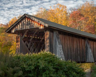 Old wooden covered bridge surrounded by autumn foliage.