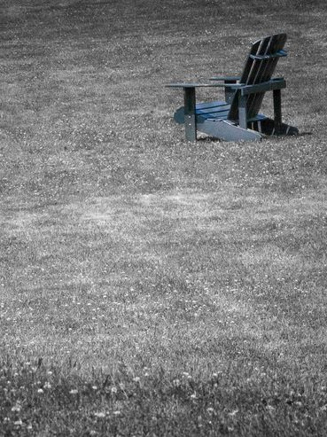 A solitary Adirondack chair in a vast grassy field.