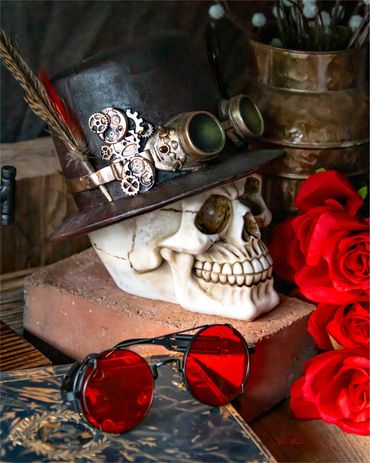 A steampunk skull adorned with a gear-trimmed hat sits beside vivid red roses and round crimson glas